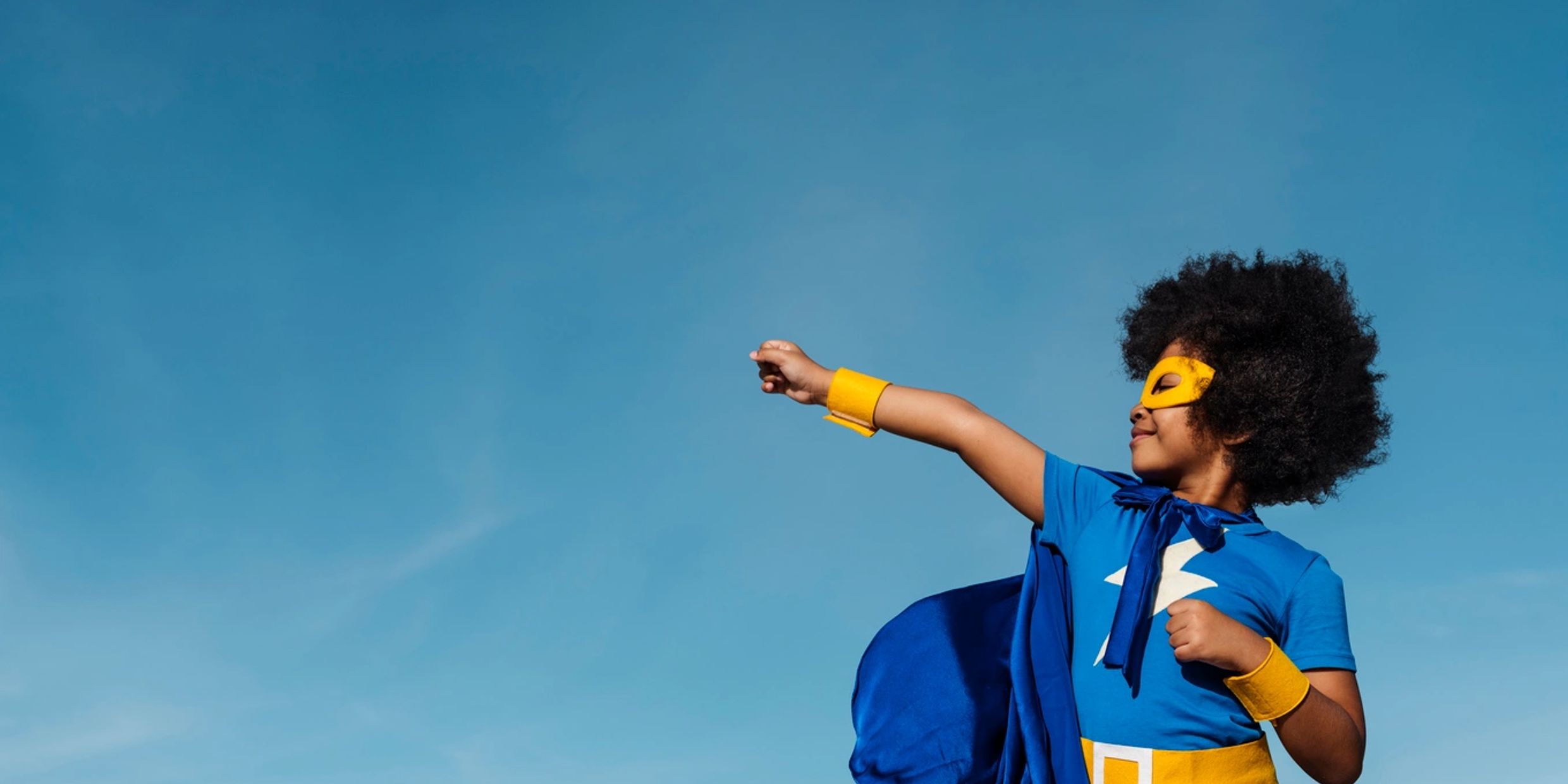 Child in a superhero costume against a blue sky